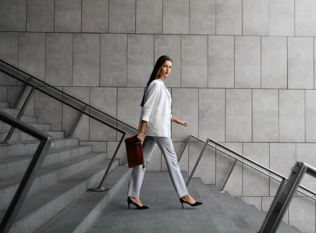 Mulher branca com terno descendo escada representando um cliente adimplente | adimplência