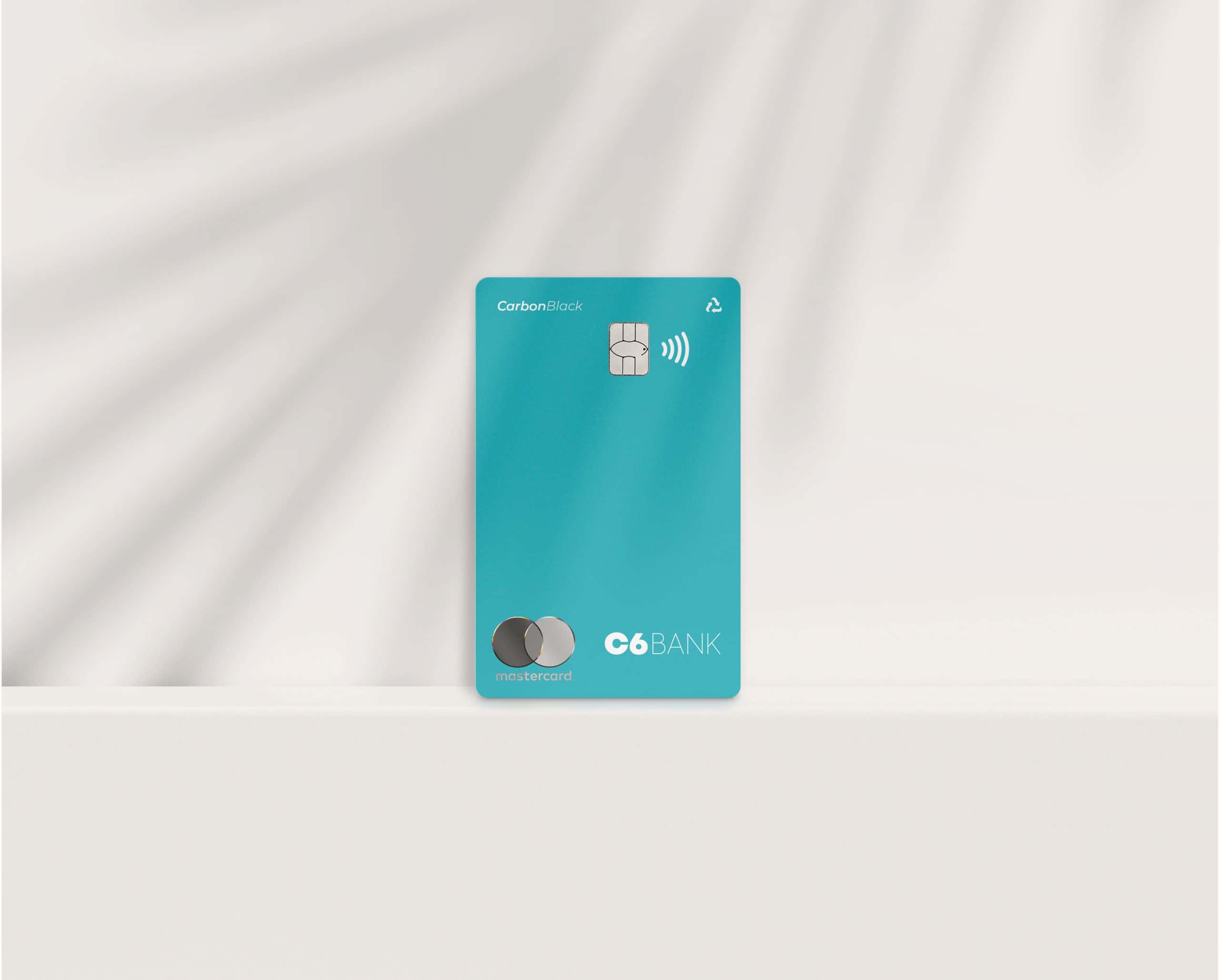 Foto do cartão Acqua, um cartão azul piscina, com o logo da Mastercard, logo do C6 Bank, a inscrição "Carbon Black", o chip, o sinal de NFC e o sinal de "retornável", posicionado em pé, em um fundo branco com efeito de movimento.