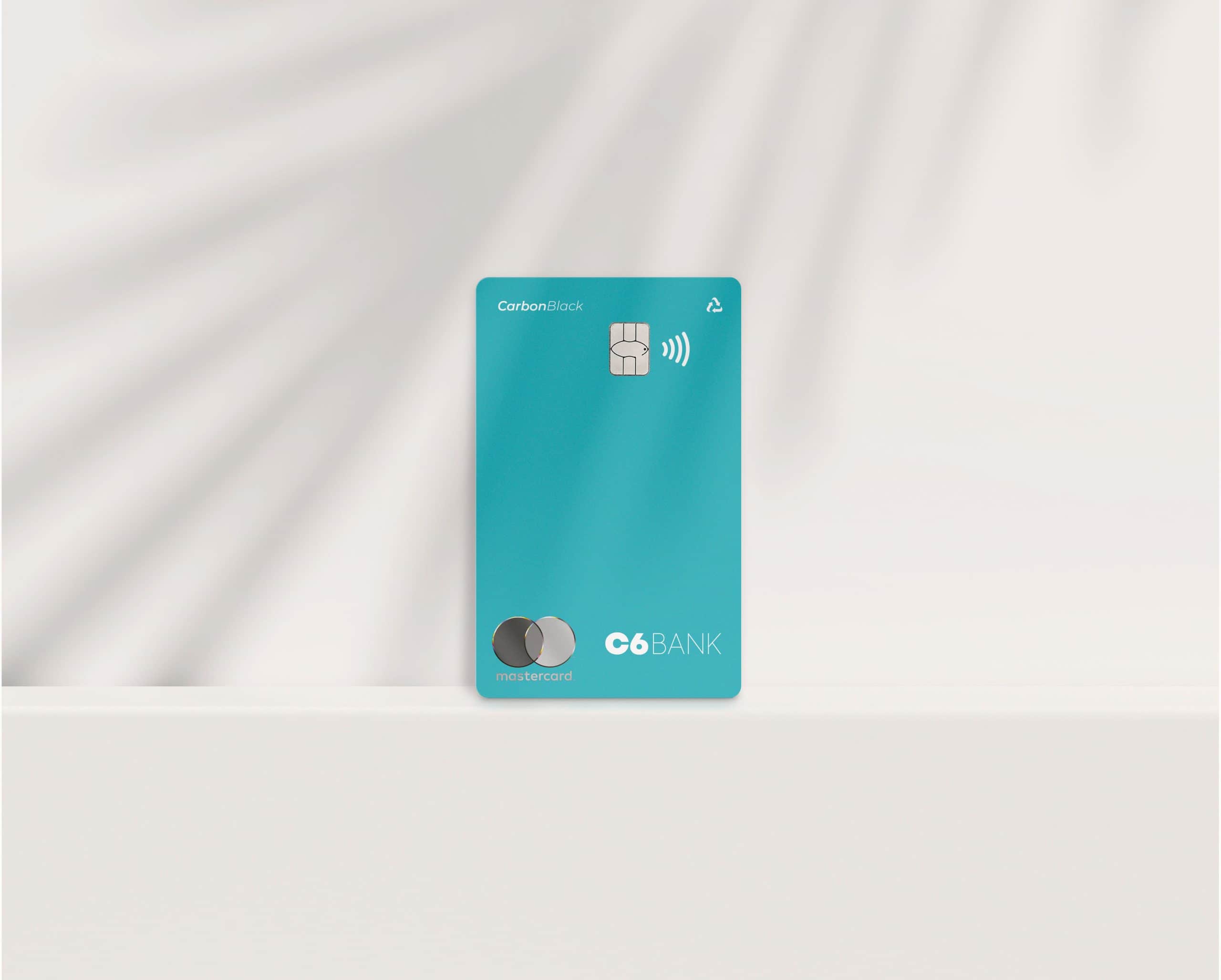 Foto do cartão Acqua, um cartão azul piscina, com o logo da Mastercard, logo do C6 Bank, a inscrição "Carbon Black", o chip, o sinal de NFC e o sinal de "retornável", posicionado em pé, em um fundo branco com efeito de movimento.