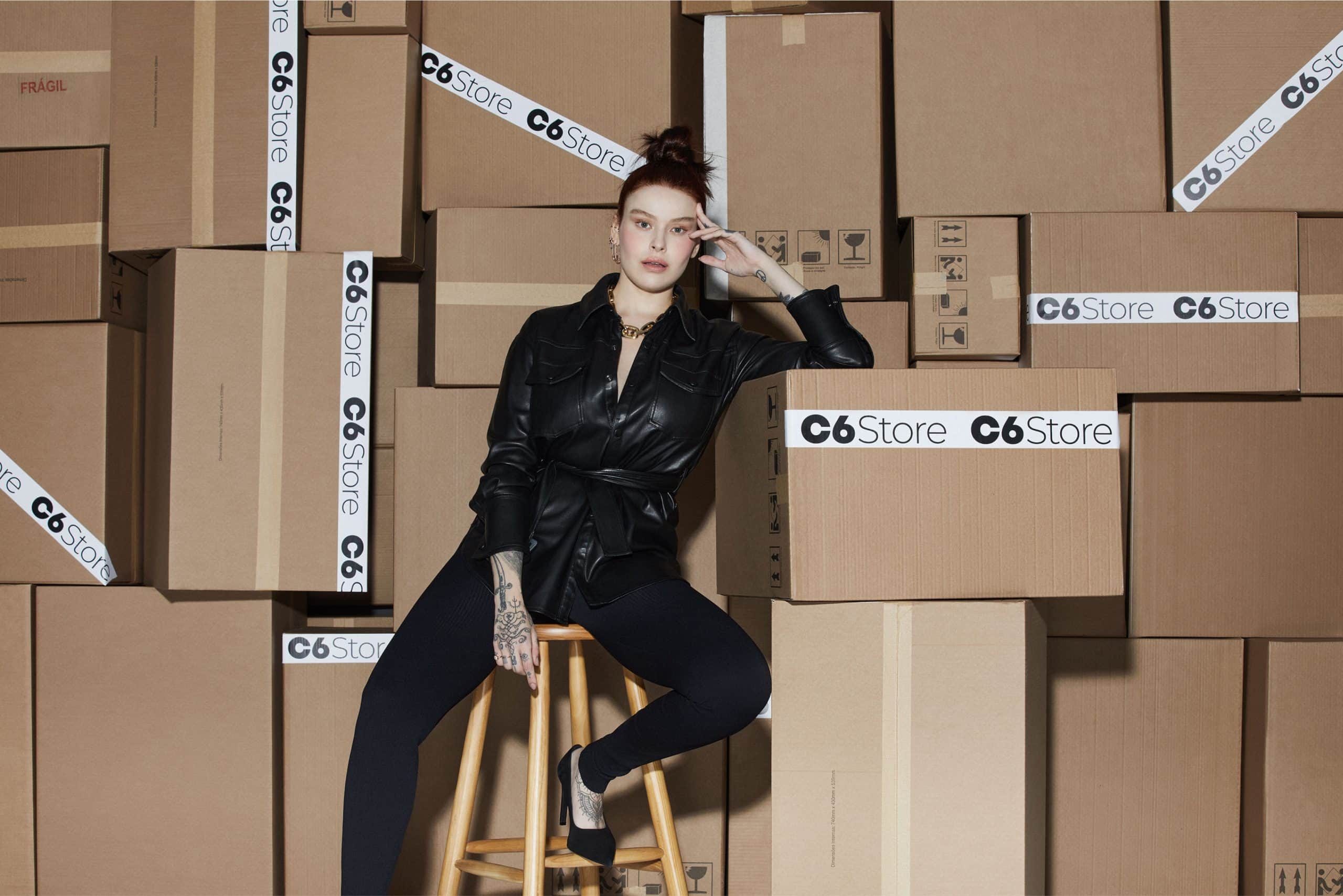 Mulher sentada ao lado de caixas com o logo do C6 Store