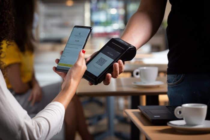 Foto de uma pessoa pagando uma conta em uma cafeteria com o C6 Bank lendo o QR Code de uma maquininha C6 Pay Smart