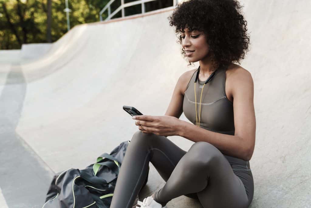Mulher negra de roupa de academia buscando no celular sobre o desconto na Reebok Sports Club para clientes C6 Bank Mastercard