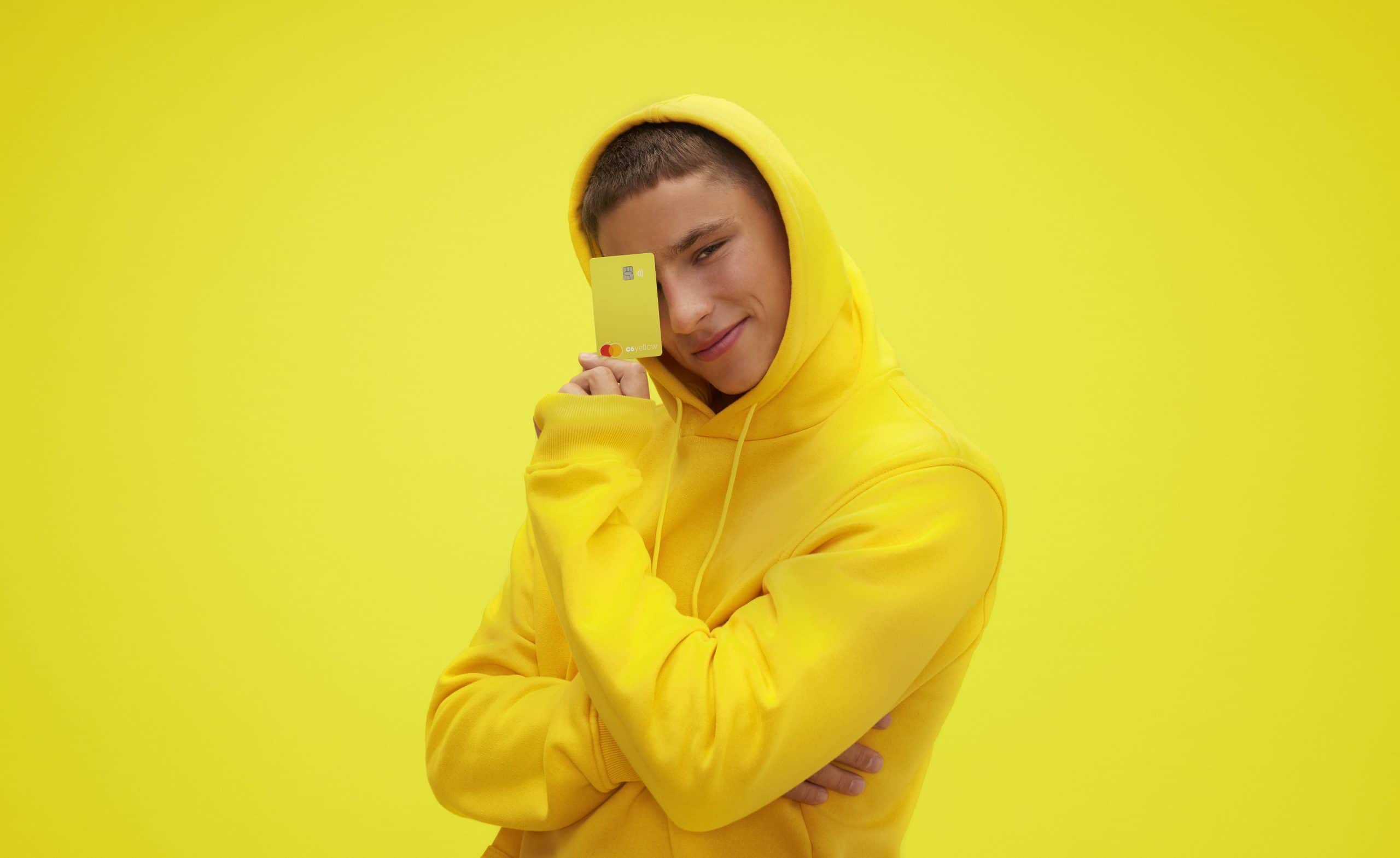 Foto de um garoto com edredon amarelo segurando um cartão também amarelo da conta Yellow num fundo amarelo.