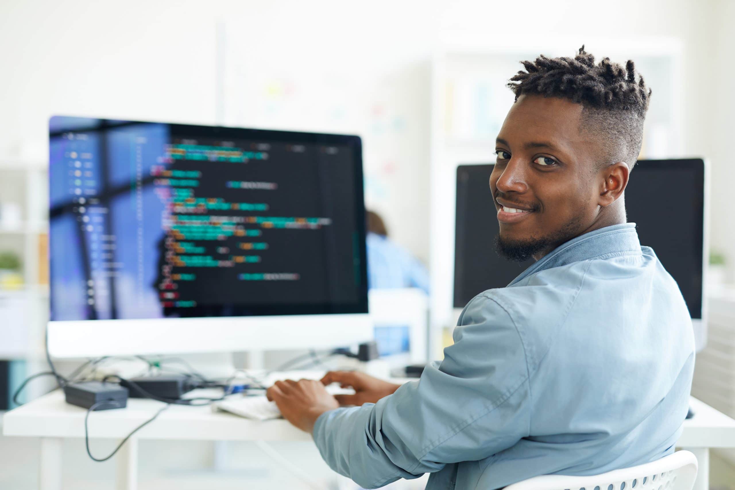 Homem negro sentando em frente ao computador olhando para trás e sorrindo